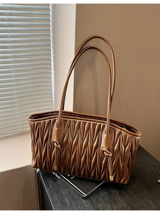 Brown vintage pleated tote bag with slim straps and drawstring detail in soft natural light