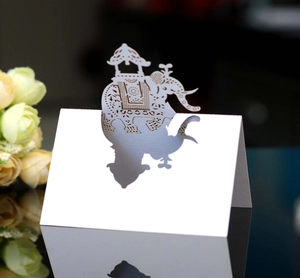 Detail of laser-cut white paper place card featuring an intricate elephant motif for weddings