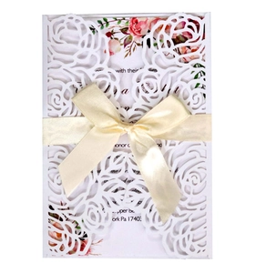 Detailed laser-cut white rose lace wedding invitation with a cream satin bow and floral insert