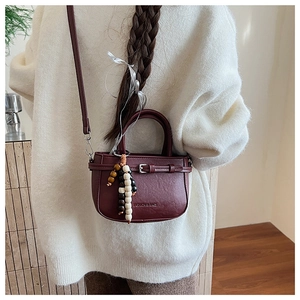 Close-up of wine red square bag with fashion buckle and decorative bead pendant detail