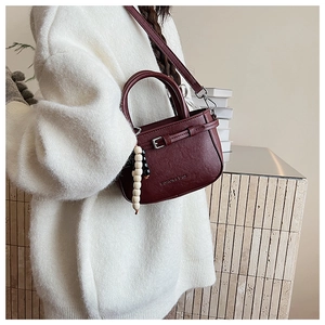 Detail of burgundy textured square crossbody bag with wood bead charm and shoulder strap