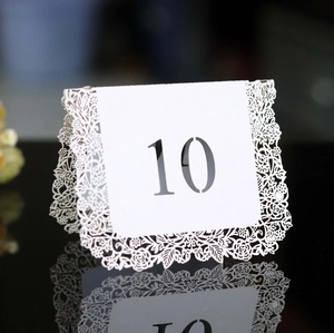 Close-up of laser-cut white lace wedding table number ten card on a black mirror