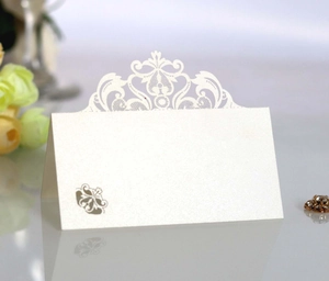 Macro detail of white lace crown place card with laser-cut hollow pattern and gold emblem
