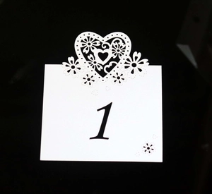 Close-up of laser-cut white wedding table card featuring intricate heart and flower lace detail