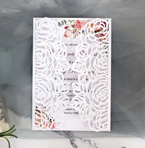 Macro detail of laser-cut white rose floral wedding invitation cover with a pink card