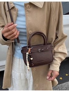 Minimalist dark brown square bag with bead tassel and strap worn with beige coat