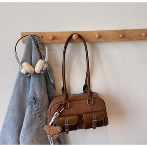 Détail du sac à épaule en daim marron avec poches à boucle et breloque ours en peluche