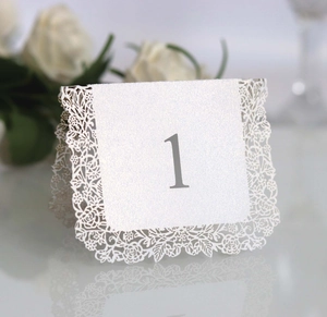 Detailed view of white laser-cut wedding table number one with elegant lace floral edges