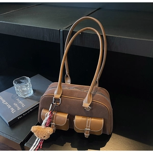 Détail d'un sac Boston en daim marron avec poches latérales et pendentif ours doux