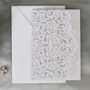 Macro detail of laser-cut floral invitations with white envelopes on marble background