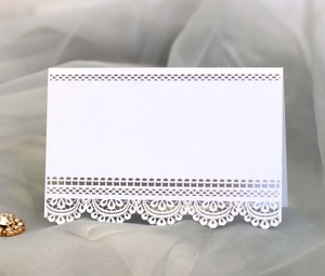 Detail of white laser-cut lace place card for weddings on elegant grey fabric