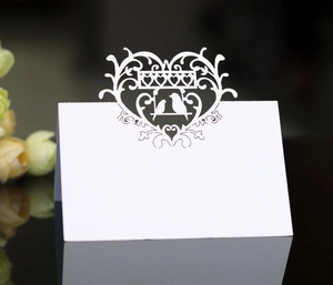 Detailed laser-cut wedding place card featuring heart and bird silhouettes on a white card