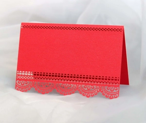 Close-up of red laser-cut place card featuring intricate lace hollowed patterns and texture