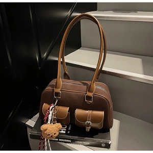 Détail d'un sac Boston en daim marron avec poches frontales et breloque ours en peluche