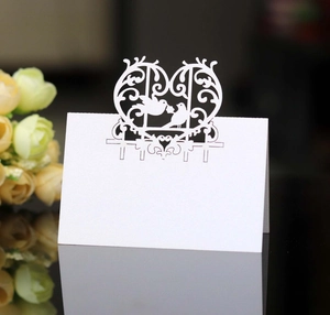 Detail of laser-cut wedding place card with heart-shaped birds design on white paper