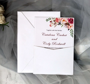 Detail of laser-cut wedding invitation with floral watercolor roses on marble surface