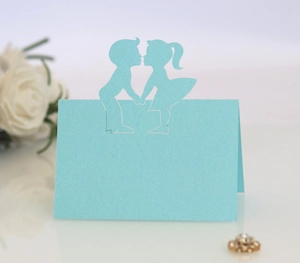 Macro detail of laser-cut light blue wedding place card featuring a boy and girl silhouette