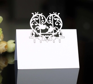 Detailed view of white laser-cut wedding place cards with heart and bird patterns