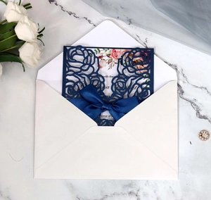 Detailed laser-cut rose patterns on navy blue wedding invitation with silk bow