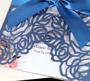 Detail of laser-cut floral pattern on navy blue wedding card with satin ribbon bow