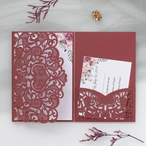 Detailed laser-cut heart pattern on burgundy wedding invitation card and floral inner leaf