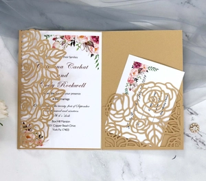 Detail of laser-cut blue rose wedding invitation with gold inner card on marble background