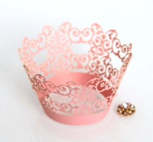 Pink laser-cut cupcake wrappers with intricate spiral lace patterns for party decoration