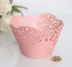 Close-up of pink laser-cut floral lace cupcake wrappers on a white surface