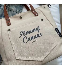 Detail of beige canvas tote bag with brown leather handle and metal rivet reinforcement