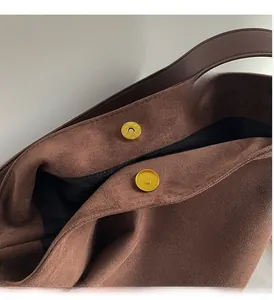 Detail of the golden magnetic buckle and suede texture on a brown shoulder bag
