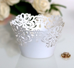 Elegant white laser-cut cupcake liners with intricate scroll patterns for wedding decor