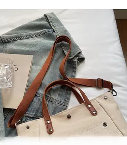 Detail of canvas tote with metal rivets, brown leather straps and adjustable shoulder strap