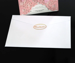 Macro view of white envelope with gold invitation sticker and pink laser-cut wedding card