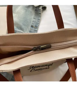 Detail view of smooth metal zipper closure and brown leather handle on canvas tote bag