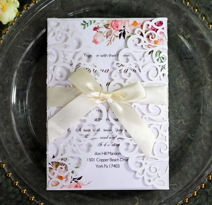 Detail of laser cut wedding invitation with cream satin bow and floral print insert