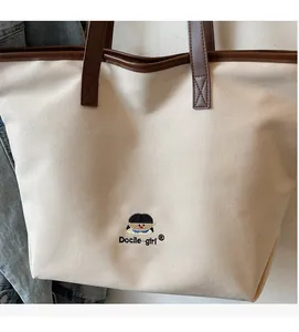 Detail of embroidered little girl and Docile girl text on off-white canvas tote bag