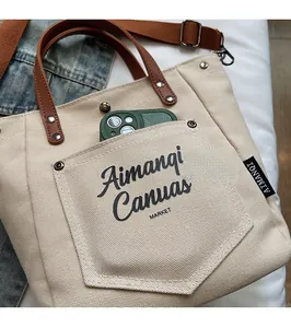 Detail of canvas tote bag showing front pocket storage for phone with leather handles