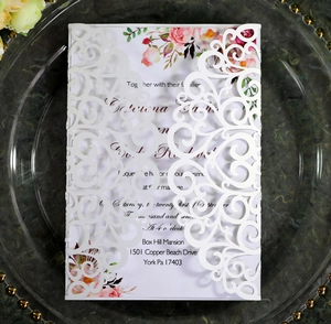 Detail of laser-cut lace wedding invitation with floral insert on a green marble backdrop
