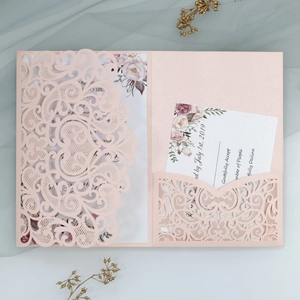 Detail of pink laser-cut wedding invitation with floral insert and RSVP card on mesh background