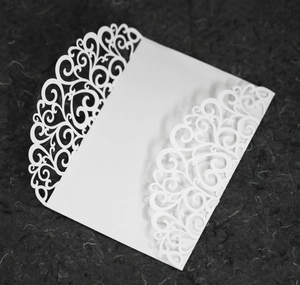 Detail of laser-cut white wedding invitation sleeve with intricate heart and floral patterns