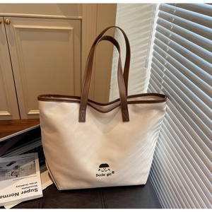 Detail of canvas tote bag showing Docile girl embroidery and brown leather trim accents