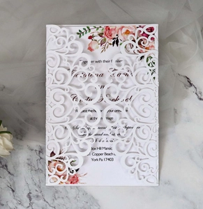 Detailed laser-cut lace wedding invitation with floral inner card on marble background