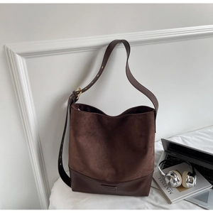 Detail of dark brown suede tote bag featuring leather stitching and adjustable strap