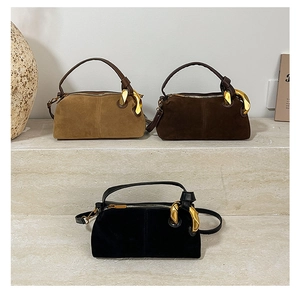 Three matte suede pillow bags in brown and black with sculptural gold handles on a stone pedestal
