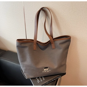 Detail of grey canvas tote with brown leather handles and reinforced stitching