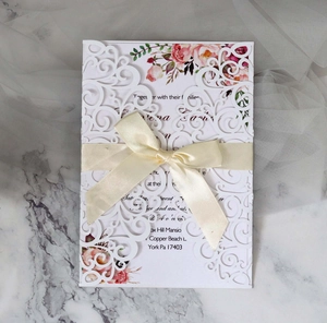 Detailed laser cut white lace wedding invitation with silk bow on marble background