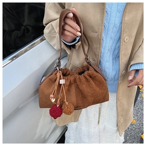 Détail d'un sac nuage en daim marron avec breloques porté sur un manteau beige