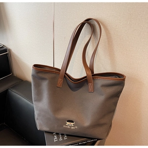Detail view of grey canvas tote bag with brown leather handles and brand embroidery