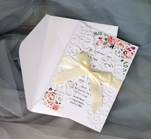 Close-up of white laser-cut lace wedding invitation with cream satin ribbon and floral insert