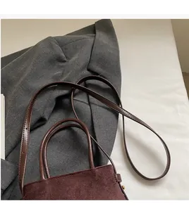 Détail du sac en daim bordeaux avec poignée en cuir marron et boucles dorées chic